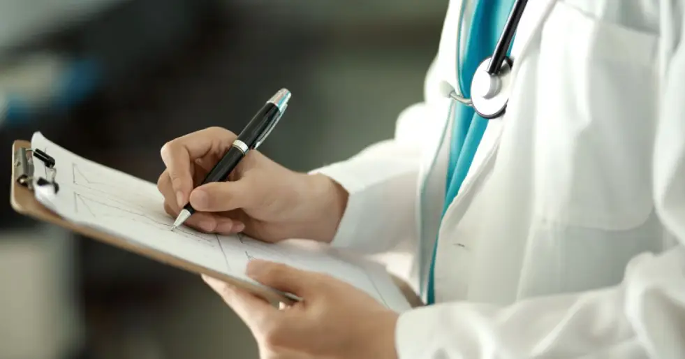 Médico escrevendo na prancheta